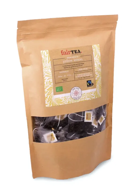 Pakke med fairtea gul sitronte med et klart vindu som viser teposer, isolert på en hvit bakgrunn.