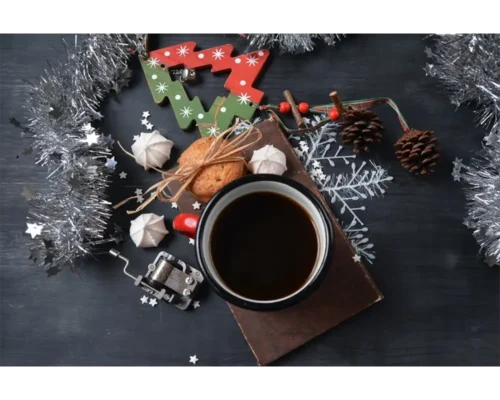 Et festlig høytidsarrangement med en kopp julekaffe, småkaker, en reinsdyrdekorasjon, kongler og sølvglitter på en mørk treflate.