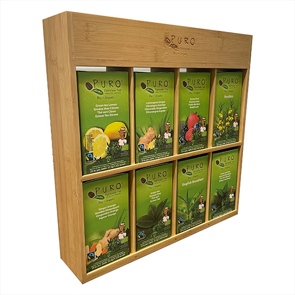 Et tredisplay inneholder åtte assorterte Puro-tebokser i to rader, hver med forskjellige smaker og grønn emballasje med bilder av ingrediensene.