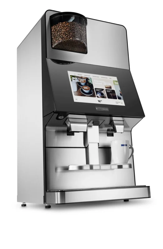 Wittenborg w100 kaffemaskin har et elegant design med en digital berøringsskjerm og to dispensere. Kaffebønner er synlige i det øverste rommet, mens et hvitt krus venter under dispenserne.