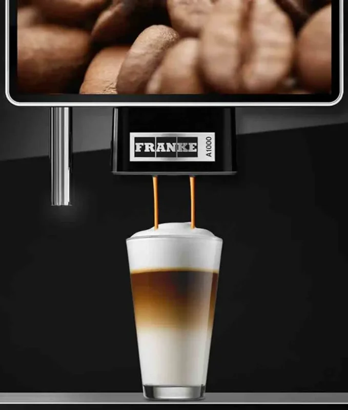 En Franke A1000 kaffemaskin som serverer en lagdelt latte i et klart glass, med kaffebønner synlige i bakgrunnen.