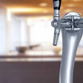 Nærbilde av en Escowa Albatross Pro 2 vanndispenser med to spaker, som heller en klar væske i et glass i en mykt opplyst bar.