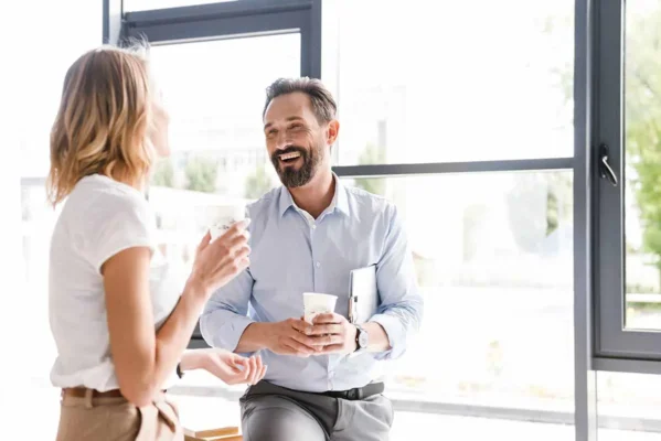En mann og en kvinne prater glade over kaffen i et lyst, moderne kontormiljø og diskuterer hvordan velge ny kaffemaskin.