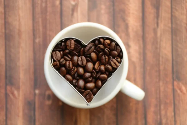 Et hjerteformet krus fylt med kaffebønner på et trebord, symboliserer et lykkelig med kaffe-øyeblikk.