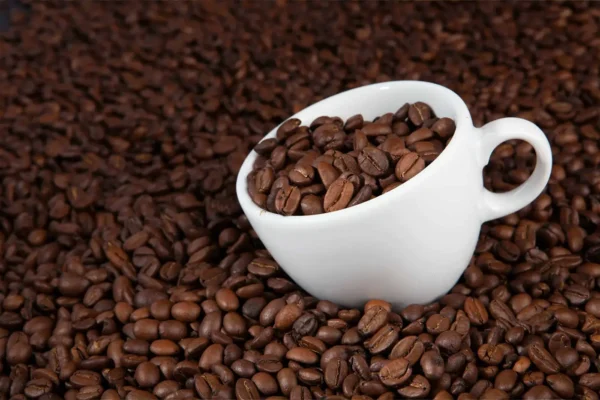Hvit kopp fylt med kaffebønner på bakgrunn av spredte kaffebønner.