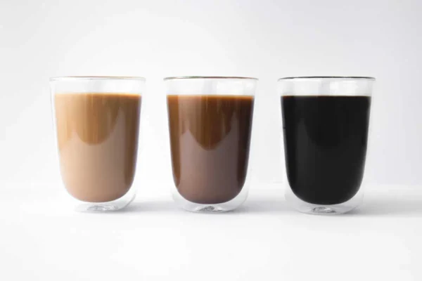 Tre glass ulike kaffetyper med varierende melkeinnhold, fra venstre til høyre: lett, medium og svart kaffe, mot hvit bakgrunn.